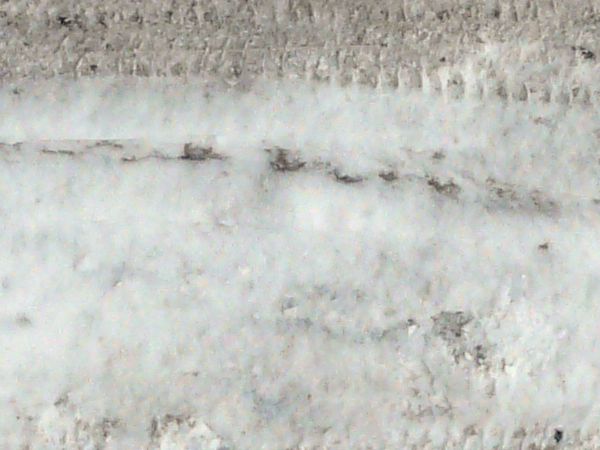 Road texture with thin layer of snow on surface and dark tire marks.